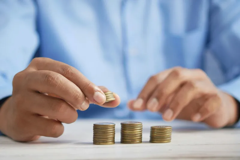Person carefully stacking coins into growing piles, illustrating capital protection